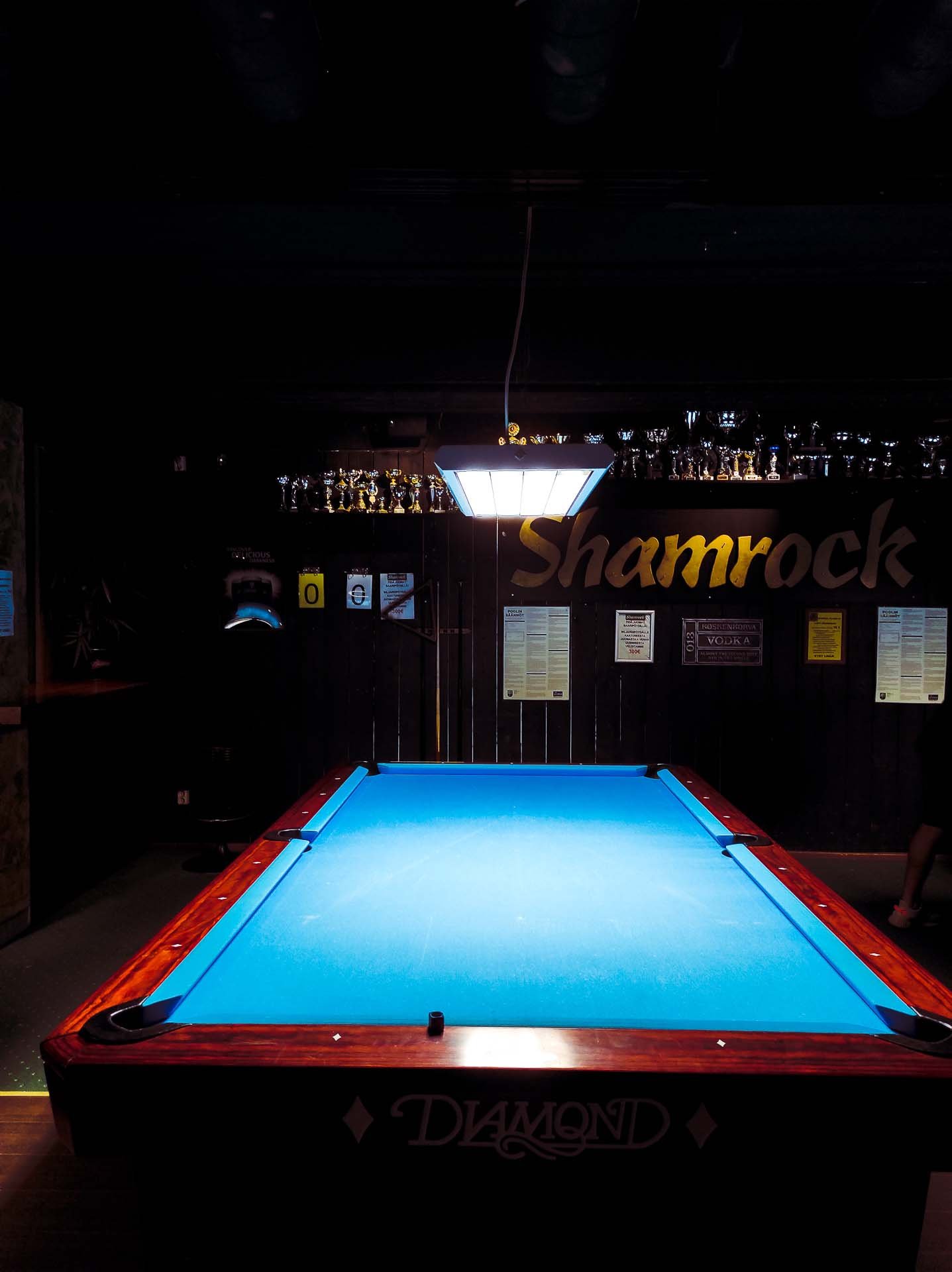 A billiard table with a lamp on top. In the background, the Shamrock logo.