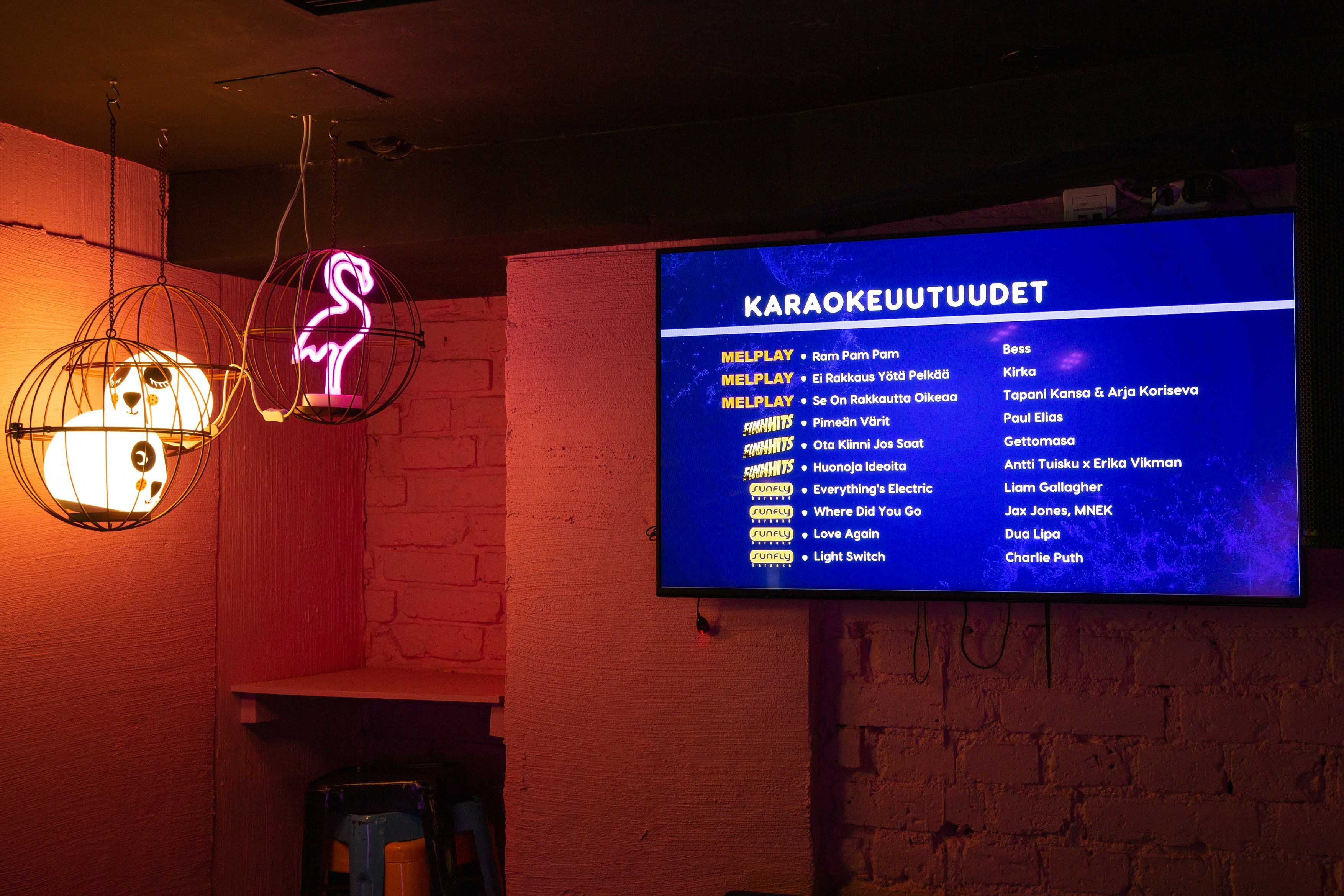 Ravintolan seinällä oleva televisioruutu, jossa näkyy karaokeuutuuksia.