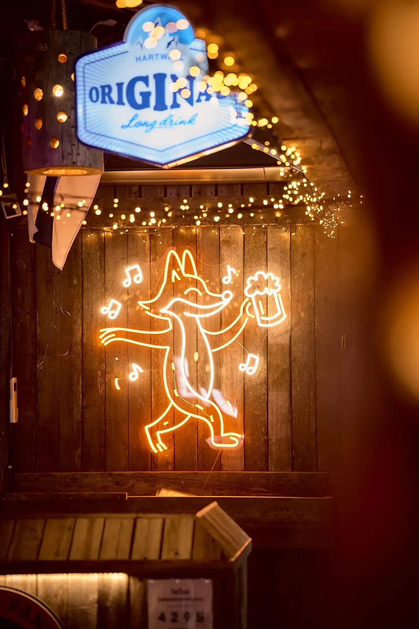 An illuminated fox mounted on a wooden wall, holding a beer mug in its paw.