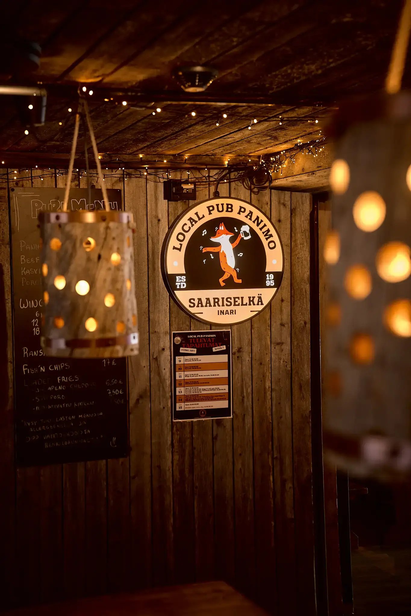 A wooden wall with a sign reading “Local Pub Panimo Saariselkä.” Warm lighting.