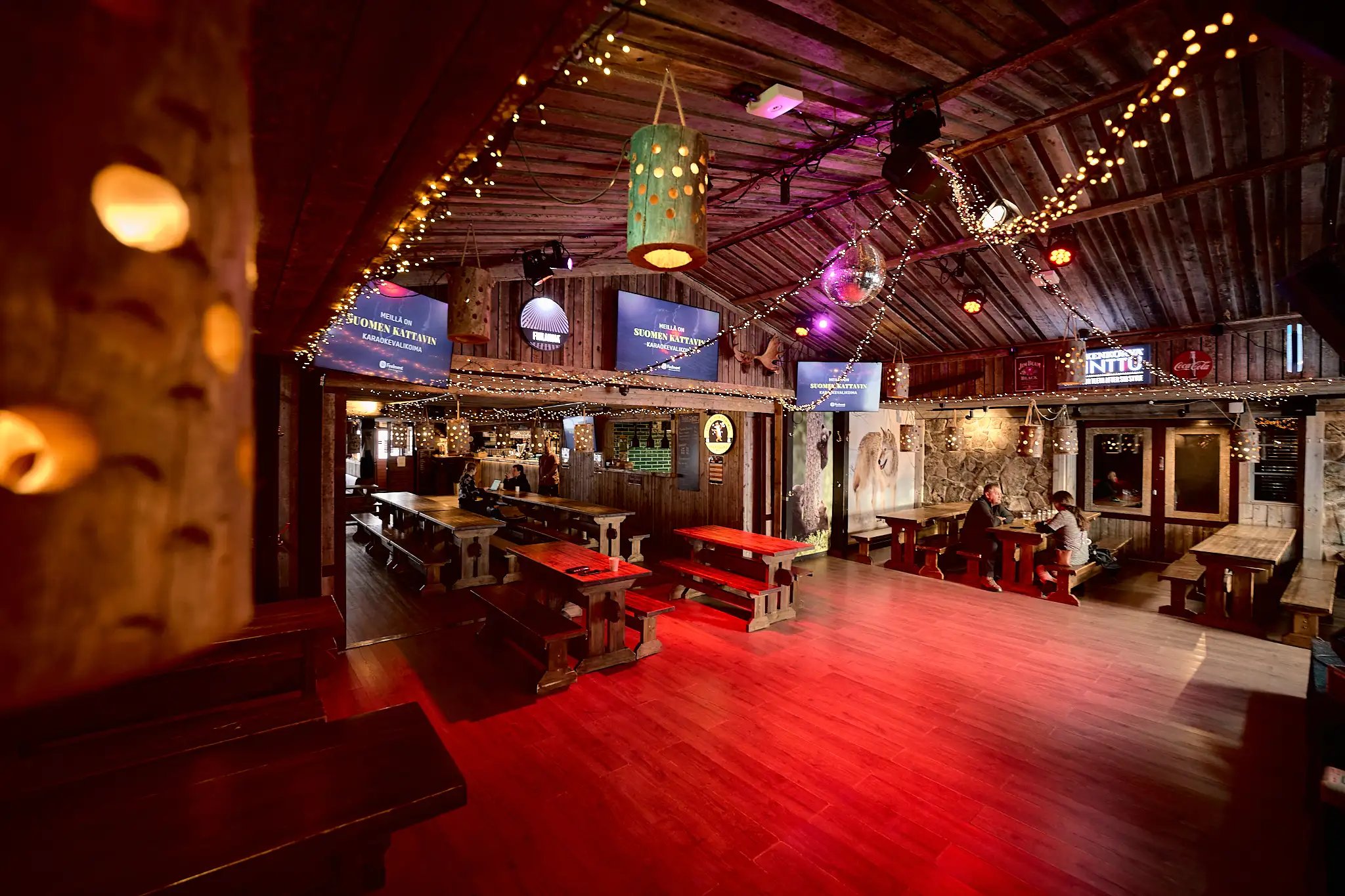 Ravintolan tanssilattia, johon heijastuu punainen valaistus. Paljon puumateriaalia ja lämmin valaistus.