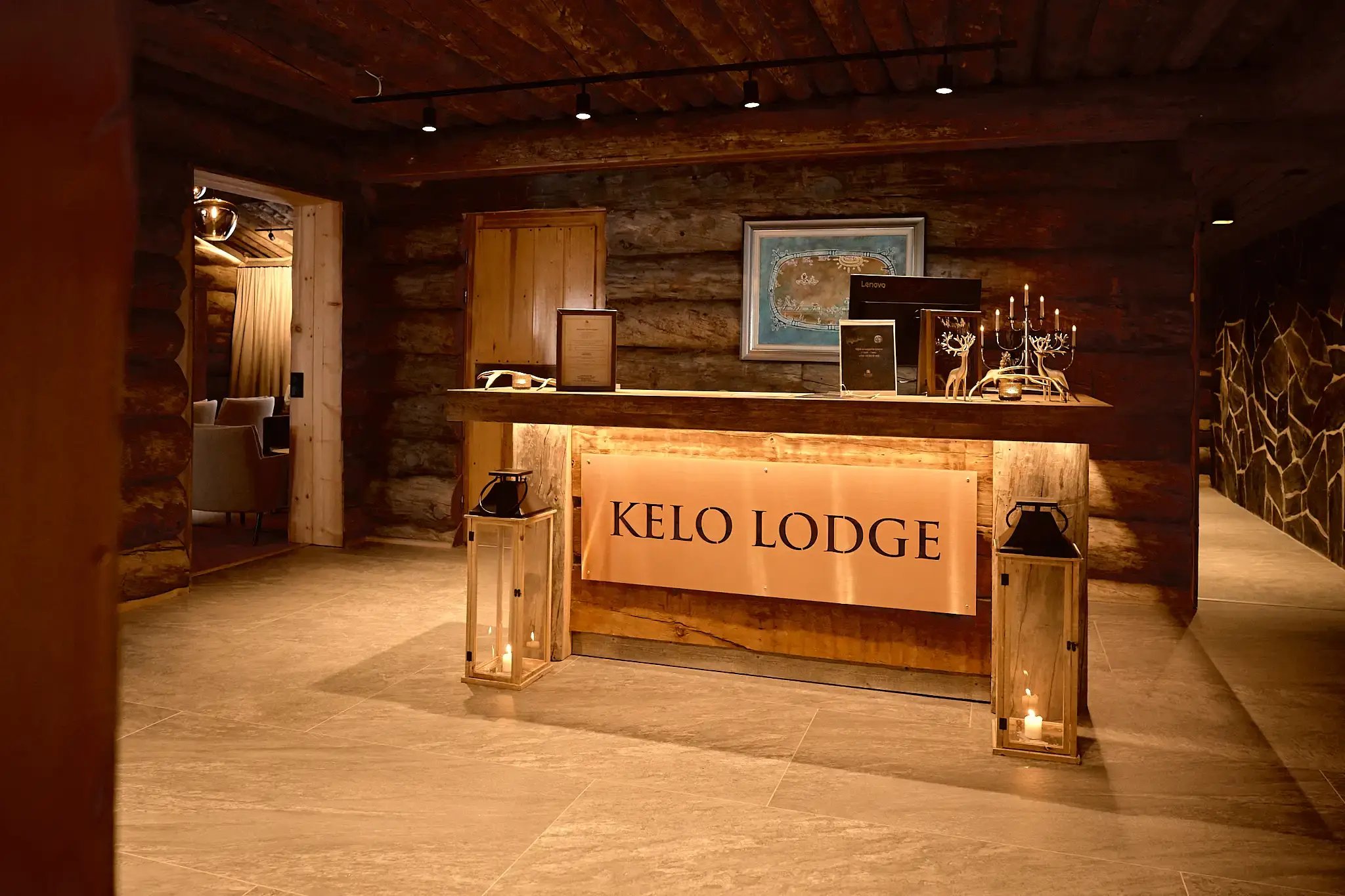 Hotellin vastaanotto. Rakennuksissa on hirsiseinät ja lämmin valaistus. Vastaanottotiskillä lukee Kelo Lodge.