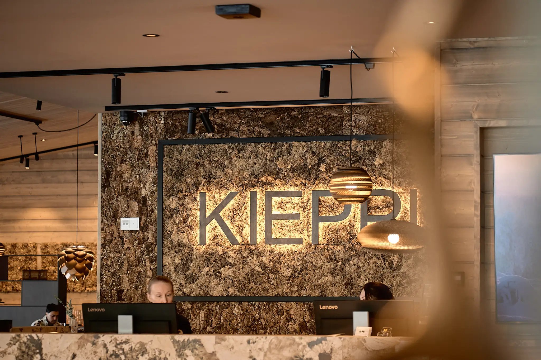 Hotellin vastaanotto. Lämmin valaistus ja takaseinällä teksti: Kieppi.