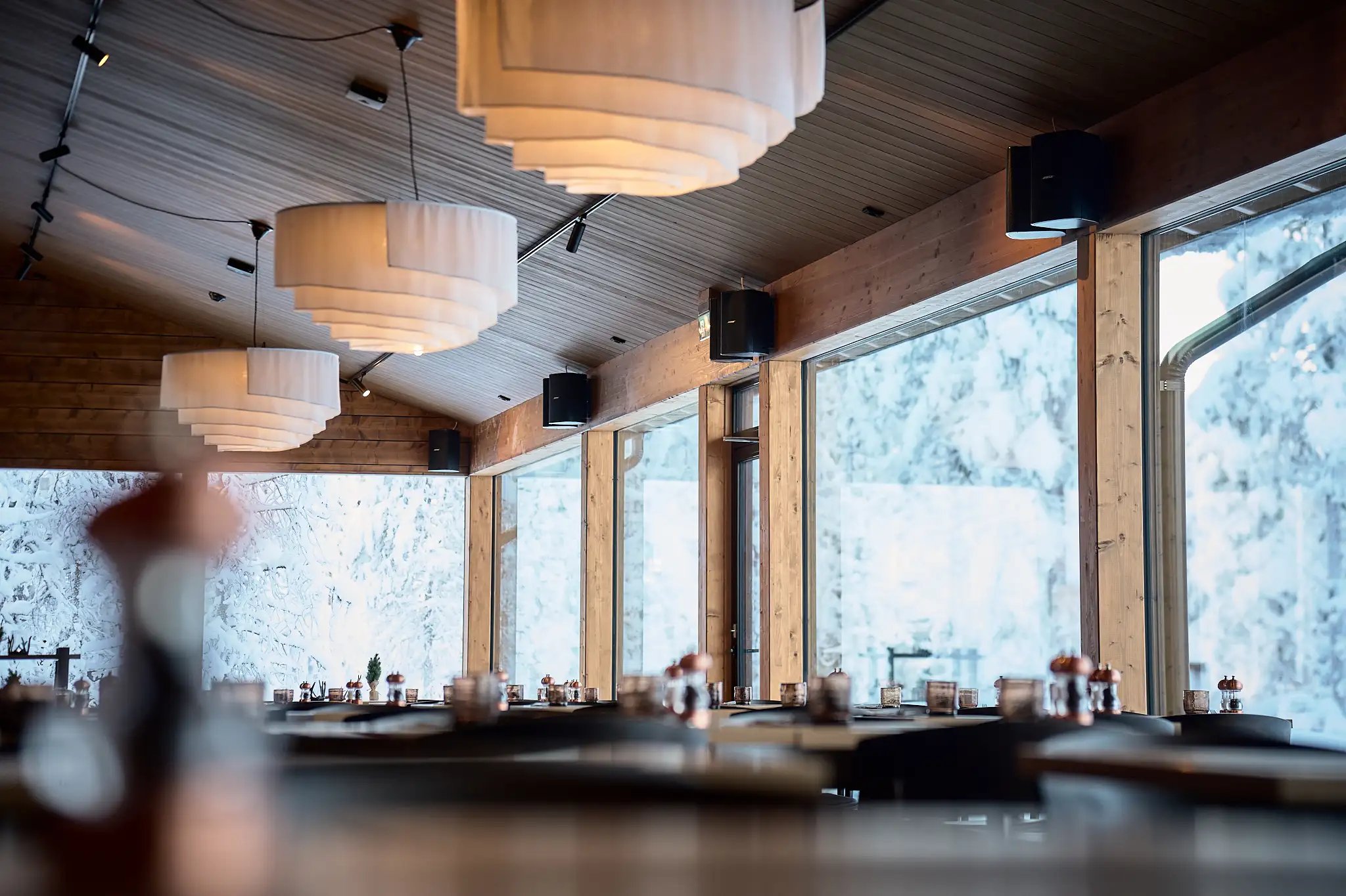 Ravintolan sisätilat. Lämmin valaistus ja isot ikkunat, joista näkyy luminen maisema.
