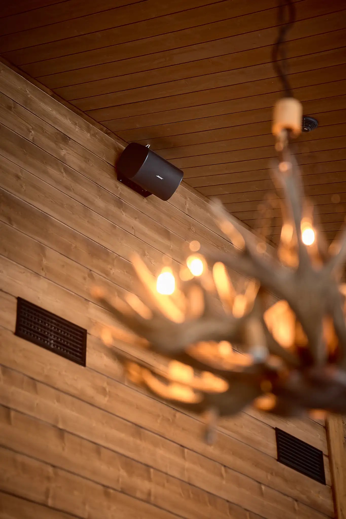 Katonrajassa oleva kaiutin, hirsiseinää sekä iso kattolamppu.