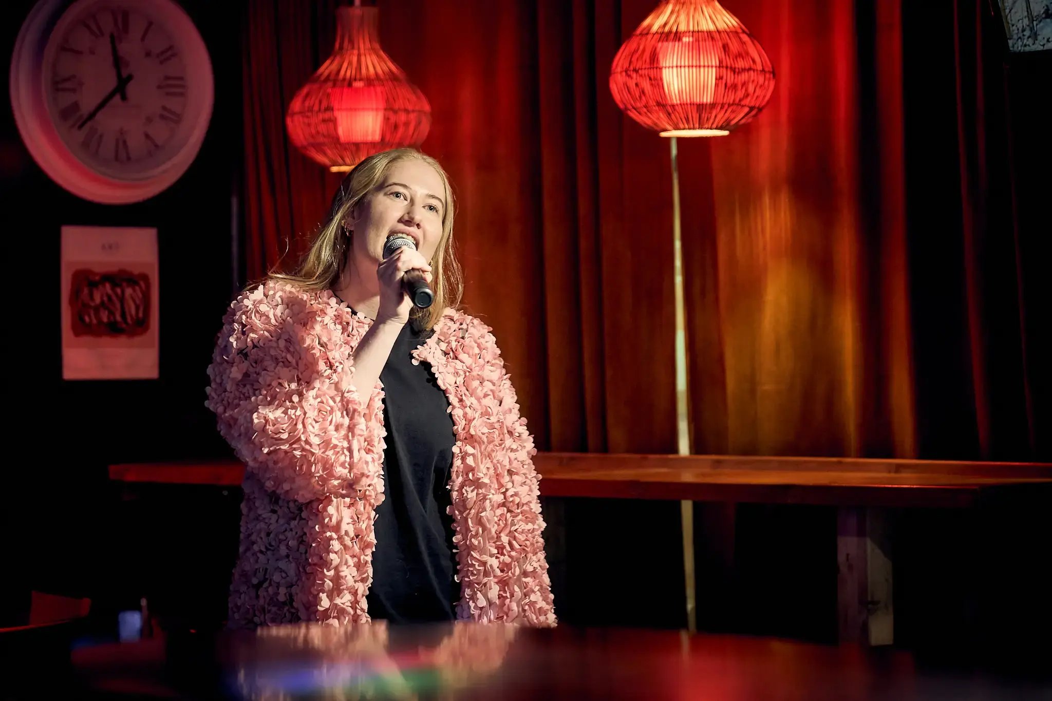 Nainen laulamassa karaokea. Punertava valaistus ja lämmin tunnelma.