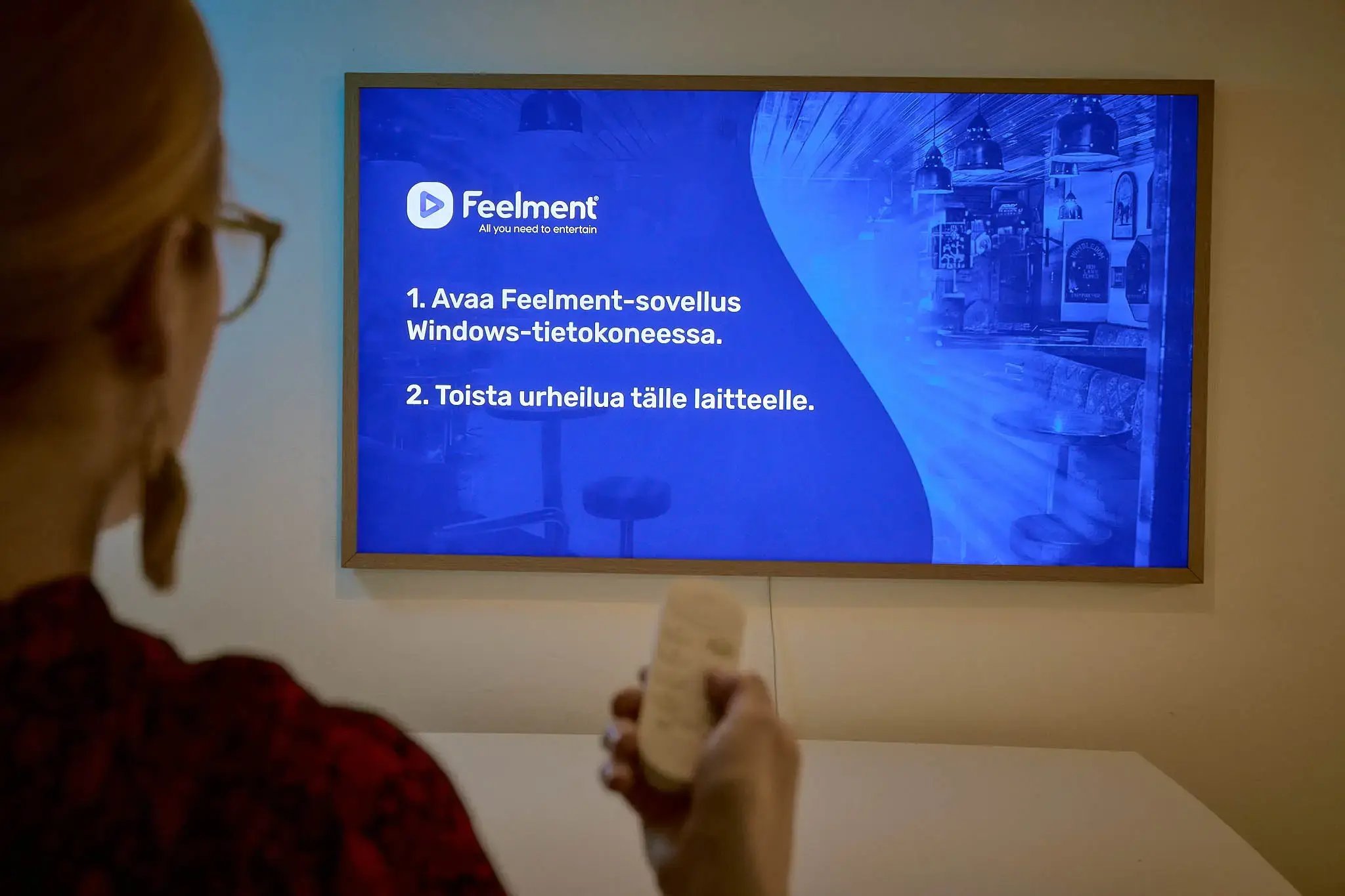 Nainen osoittamassa kaukosäätimellä tv-ruutua, jossa näkyy Feelment TV -sovellus.