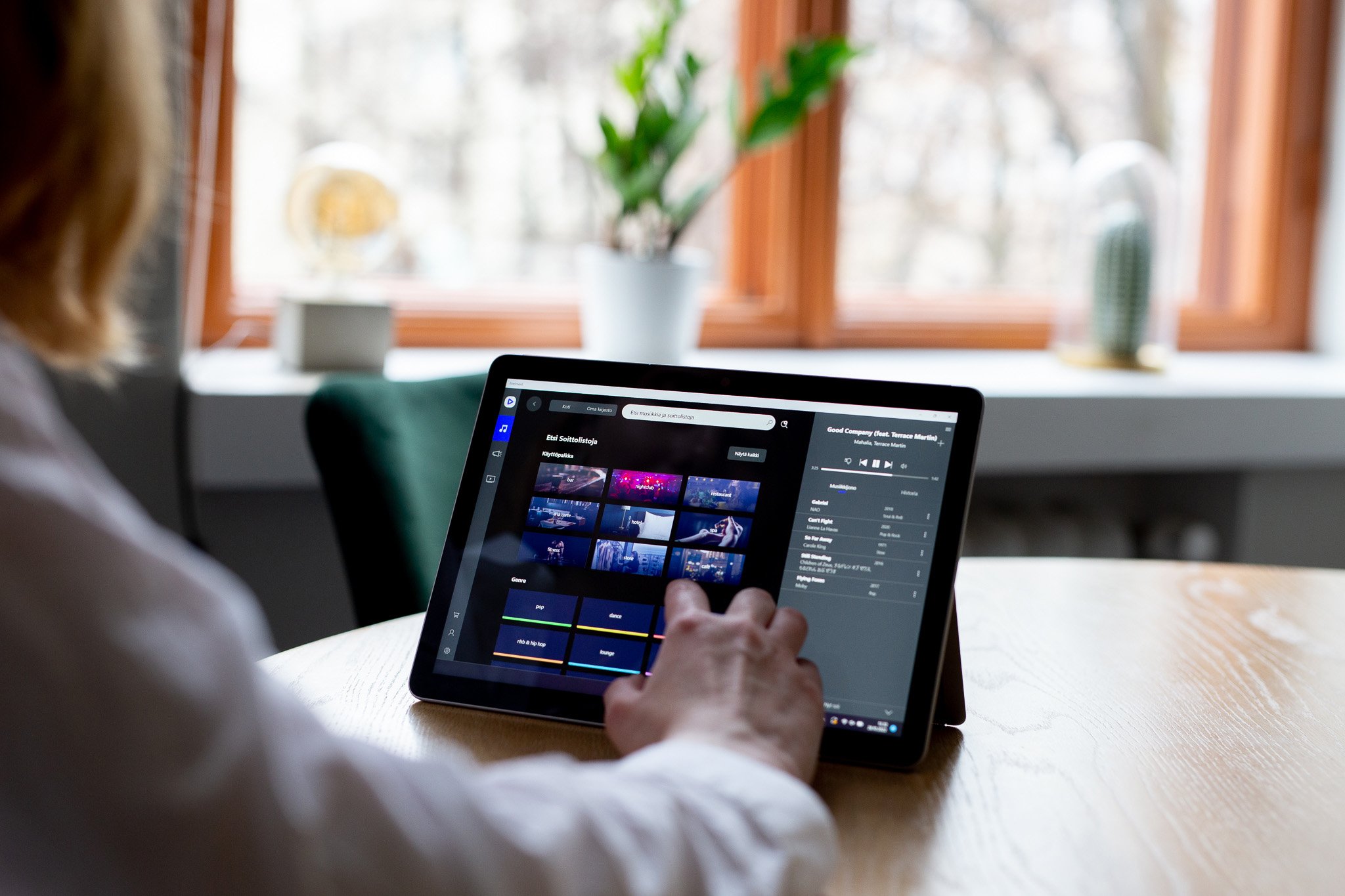 Nainen käyttämässä tablettia, jossa on päällä Feelmentin musiikkisovellus. Taustalla ikkuna ja viherkasvi.