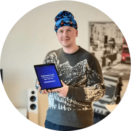 A male person wearing a hat and a sweater. Holding a tablet with the text Feelment-support on the screen.