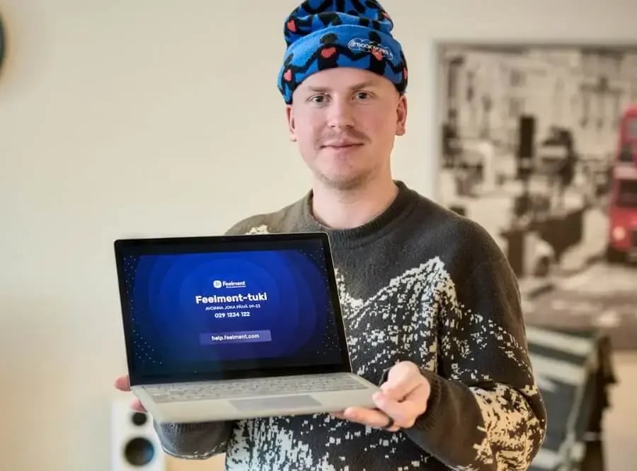 Pipopäinen mieshenkilö pitelemässä läppäriä käsissään. Läppärin näytöllä teksti 