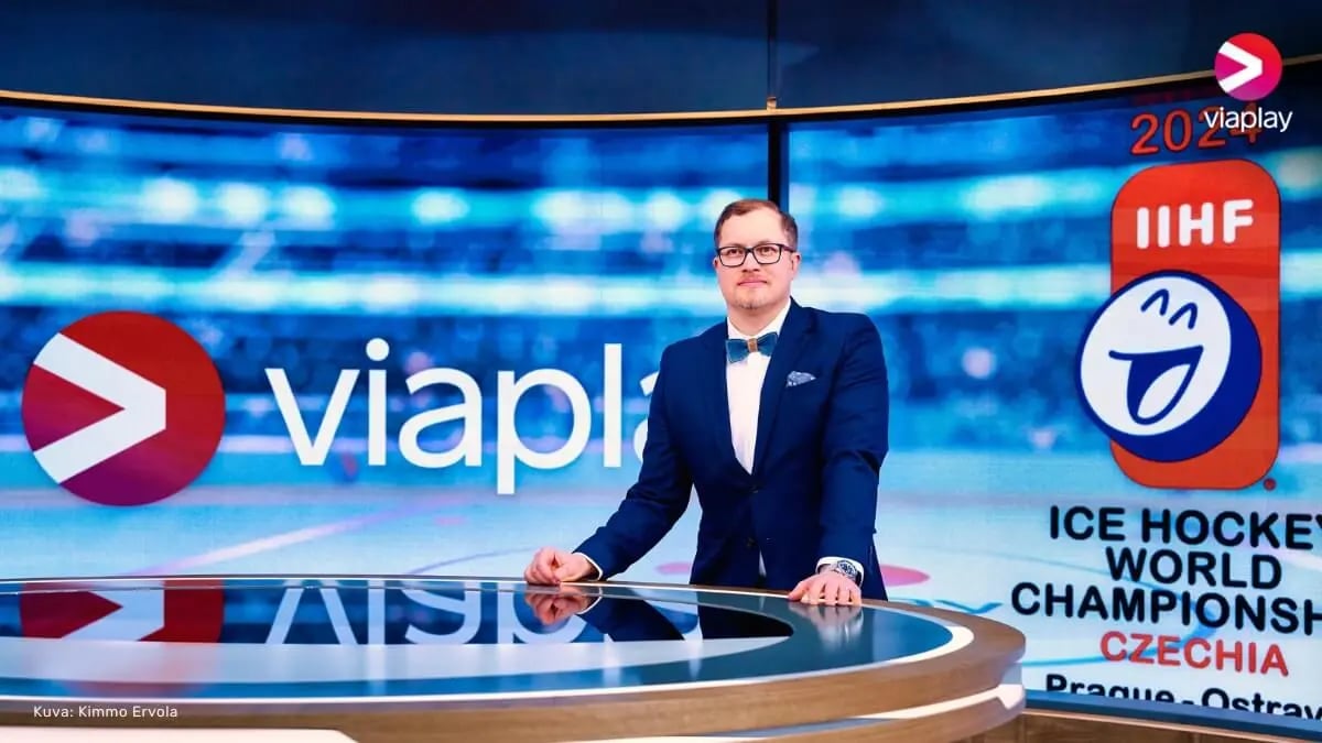 Viaplay commentator Antti Mäkinen standing in the studio behind a table. In the background, there is a large screen displaying Viaplay and Ice Hockey World Championships logos.
