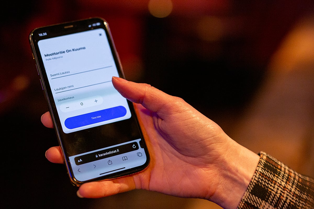 Feelment karaokelistat palvelu puhelimen näytöllä, joka on naisen kädessä ravintolassa
