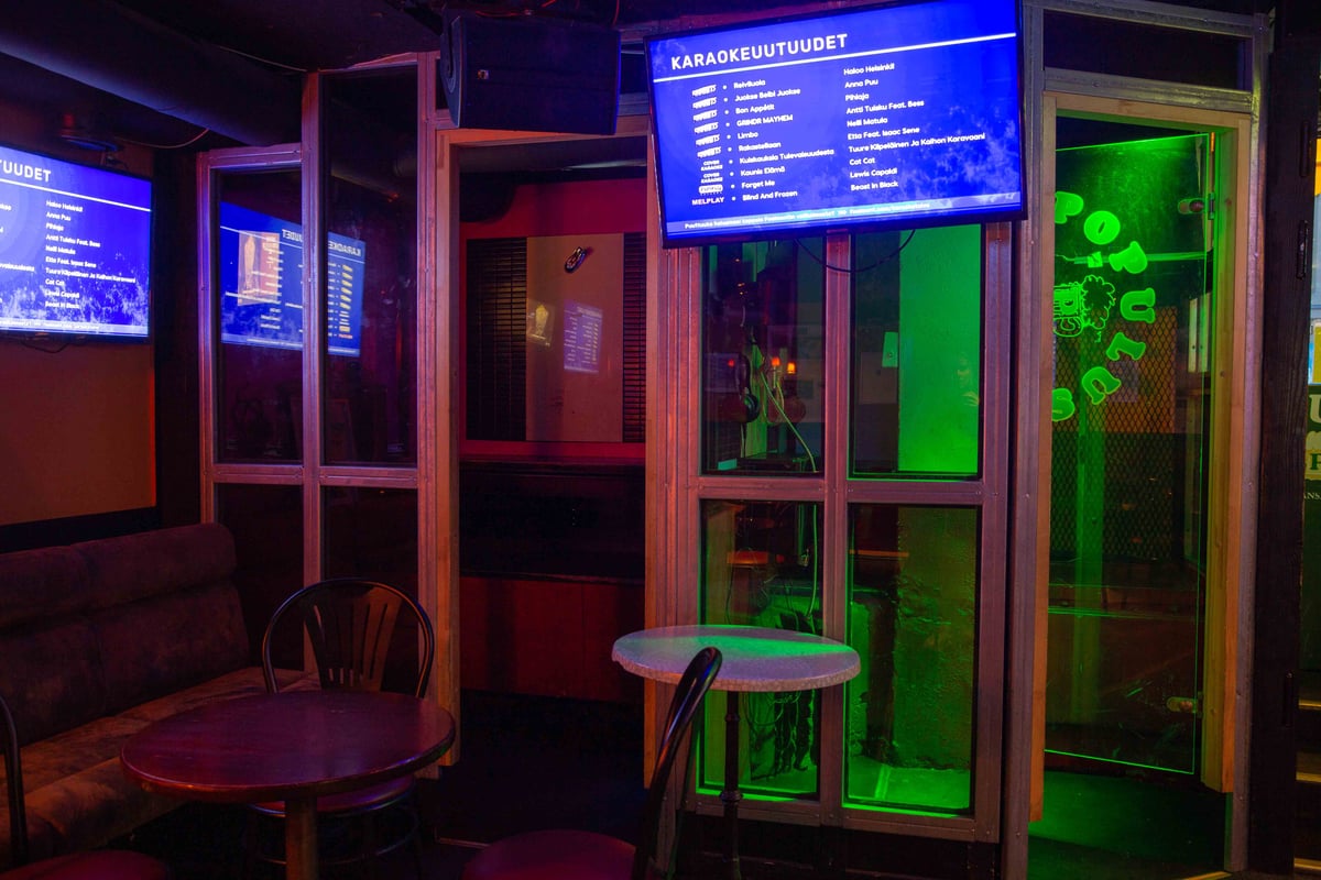 Feelment karaokeravintola, jonka seinillä televisioita joissa mainostetaan karaokeuutuuksia. Taustalla kaksi karaokekoppia itsepalvelukäyttöön