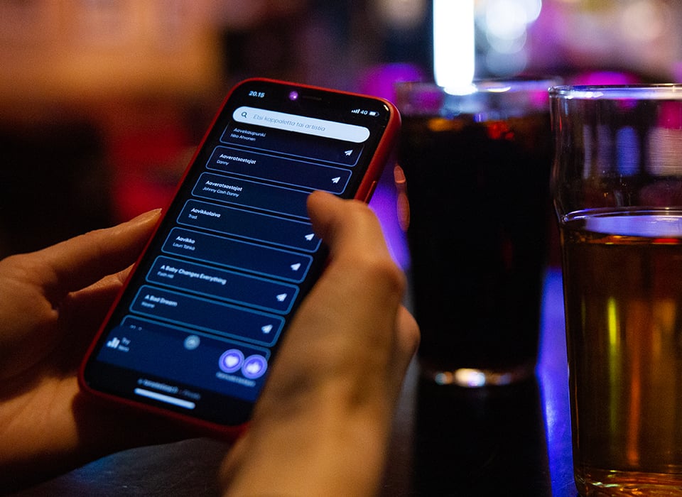 A phone in someone's hand displaying a list of karaoke songs. Two beer mugs beside it.