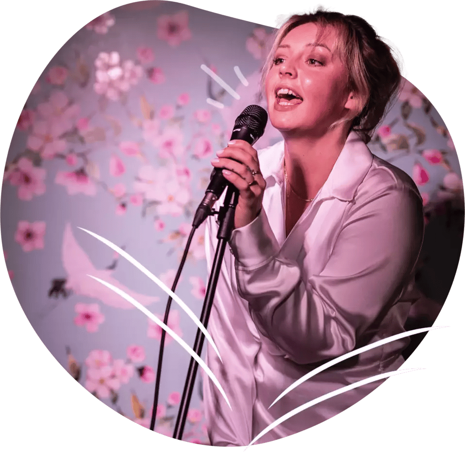 Nainen laulamassa karaokea. Taustalla vaaleanpunainen seinä, jossa kukkia ja lintuja.