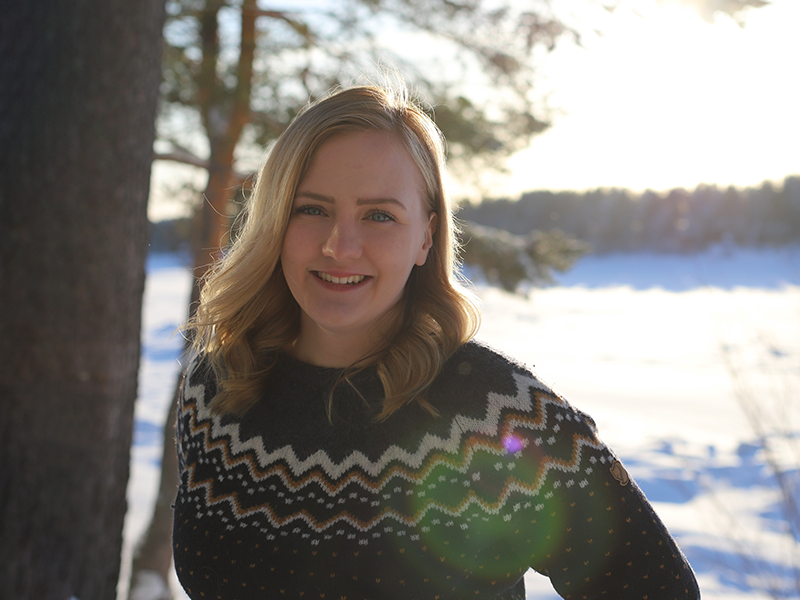 A smiling young woman standing next to a tree with a wintery backgrond.