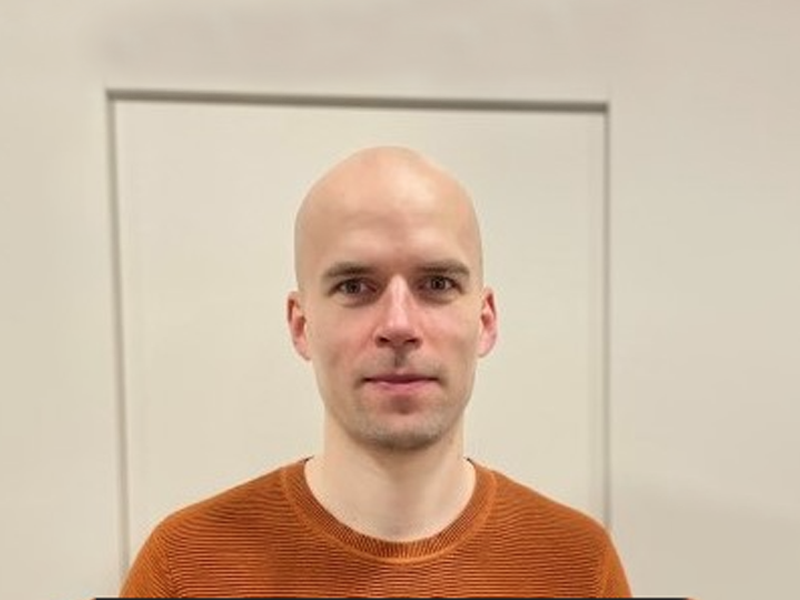 A bald man wearing an orange shirt, white background. 