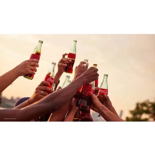 Ihmisiä kippistämässä lasisten CocaCola-pullojen kanssa.