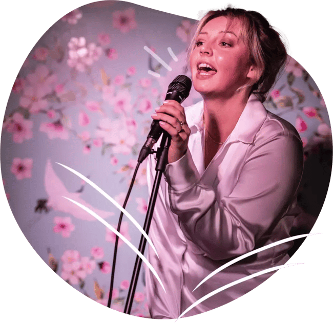 Vaaleanpunaiseen paitaan pukeutunut nainen laulaa Feelment karaokea