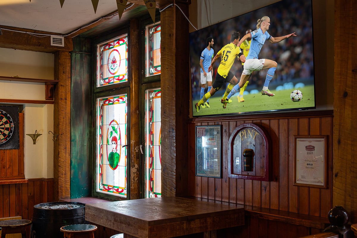 Restaurant interior with a television mounted on the wall, showing a live football match.