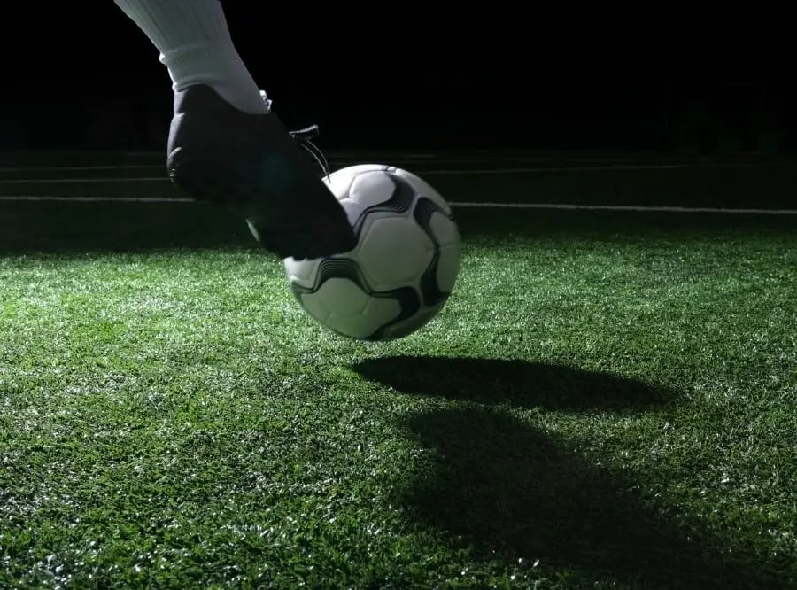 Henkilö potkaisemassa jalkapalloa viheriöllä.