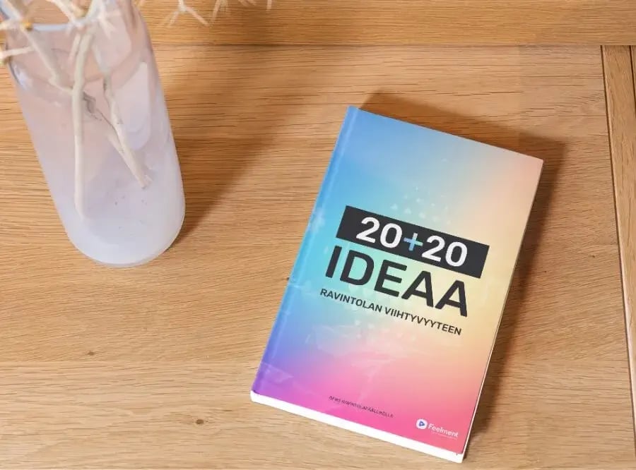 Ruskealla pöydällä oleva kirja, jonka kannessa teksti 20 + 20 ideaa ravintolan viihtyvyyteen.