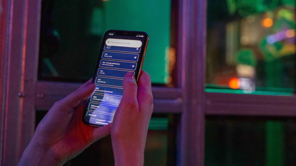 Kädet pitelemässä älypuhelinta jossa näkyy lista karaokekappaleista.