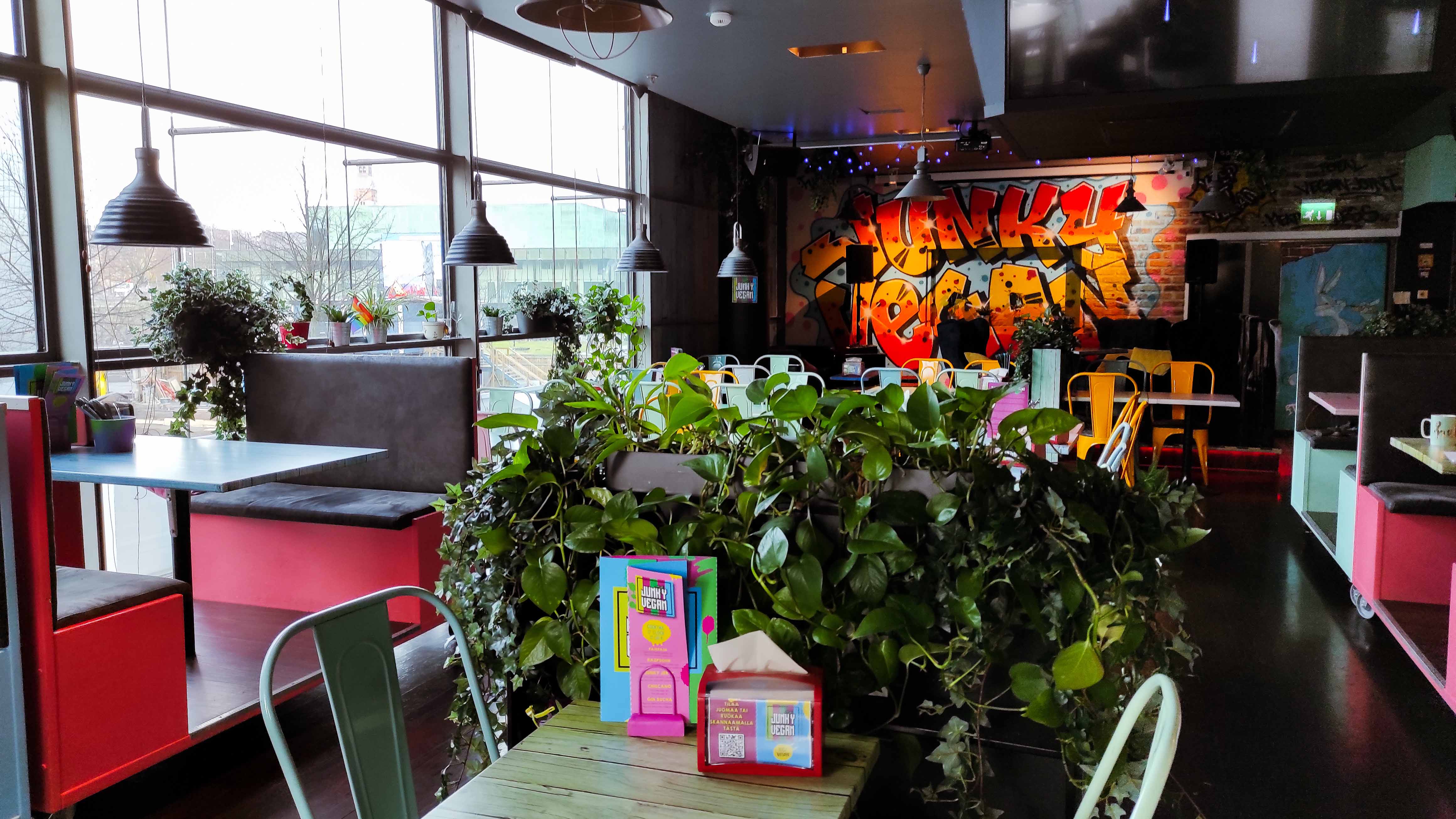 Tables and chairs in the restaurant. In the background, green plants, and on the wall, colorful graffiti.