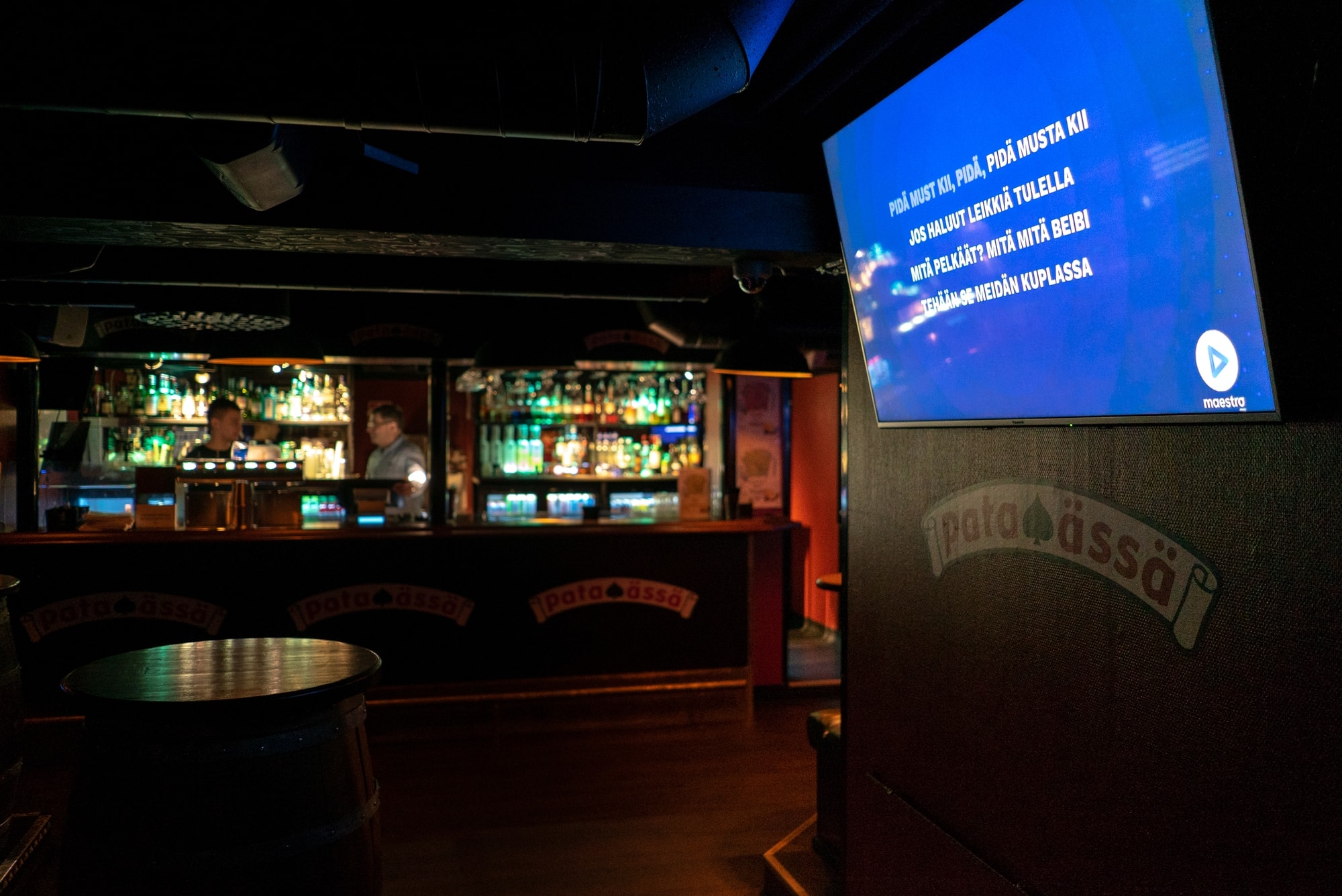 Karaokebaarin sisätila. Taustalla baaritiski ja seinällä TV-ruutu, jossa pyörii karaokea.