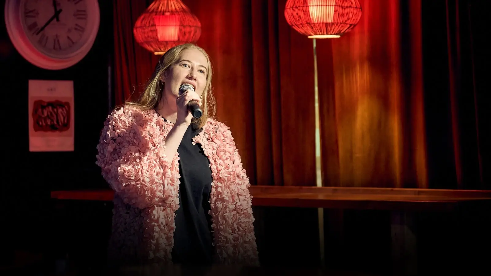 A woman singing karaoke. Red lamps in the background. Warm lighting.