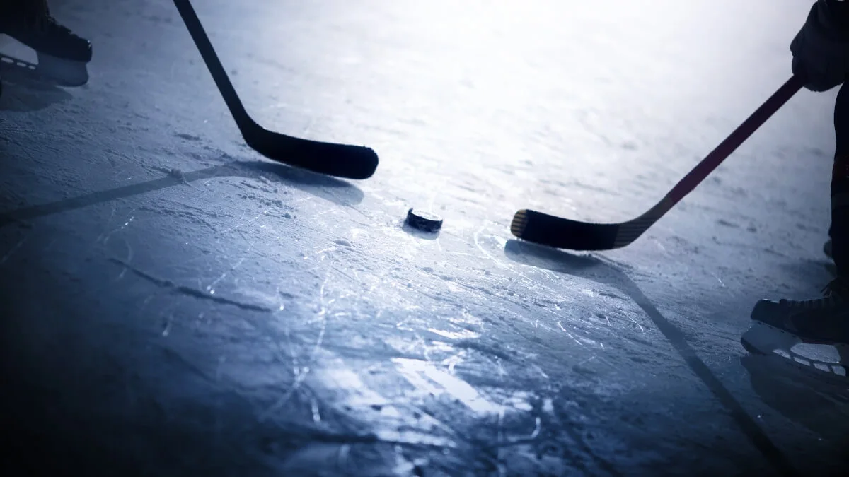 Two ice hockey sticks and a puck on the ice, photographed up close