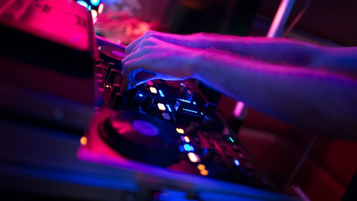 Ihmisen kädet, jotka säätävät DJ-pöydän nappuloita. Hämärä, sinisenvioletti valaistus.