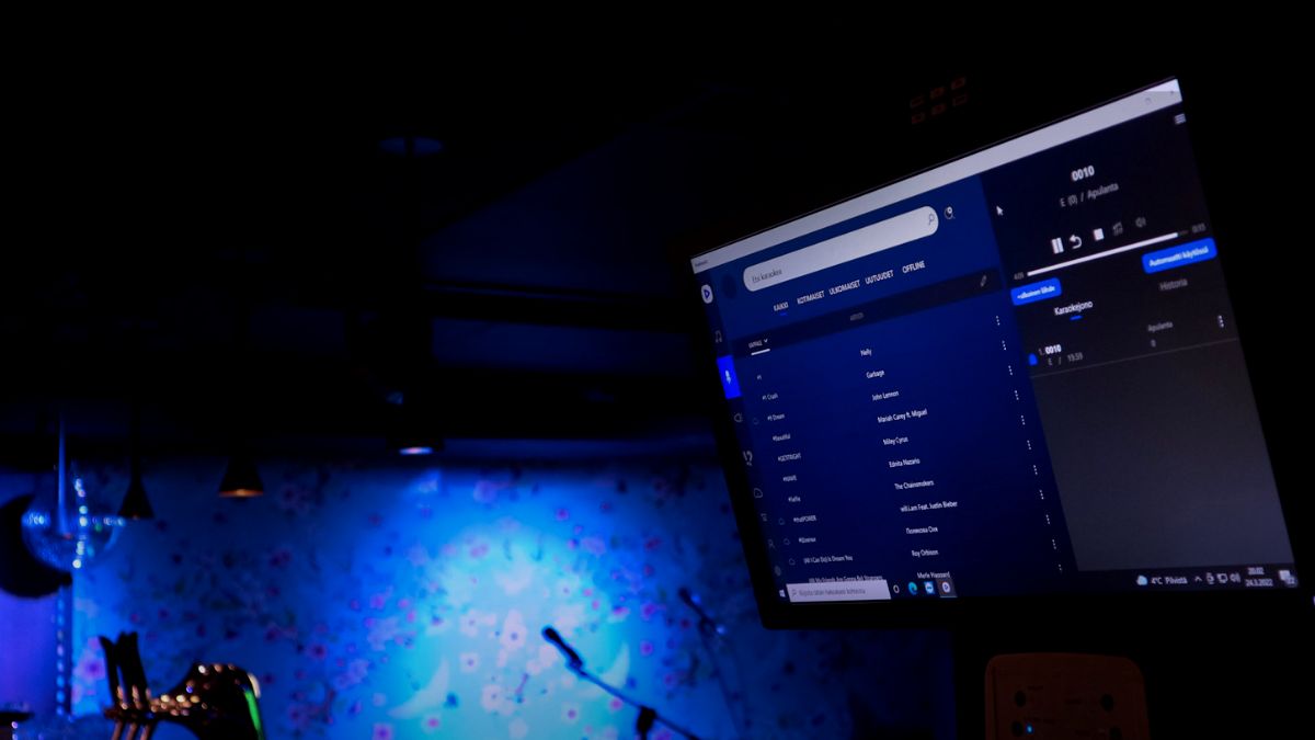 Tietokoneen näyttö, jossa näkyy Feelmentin sovellus. Taustalla karaokemikki ja -lava.