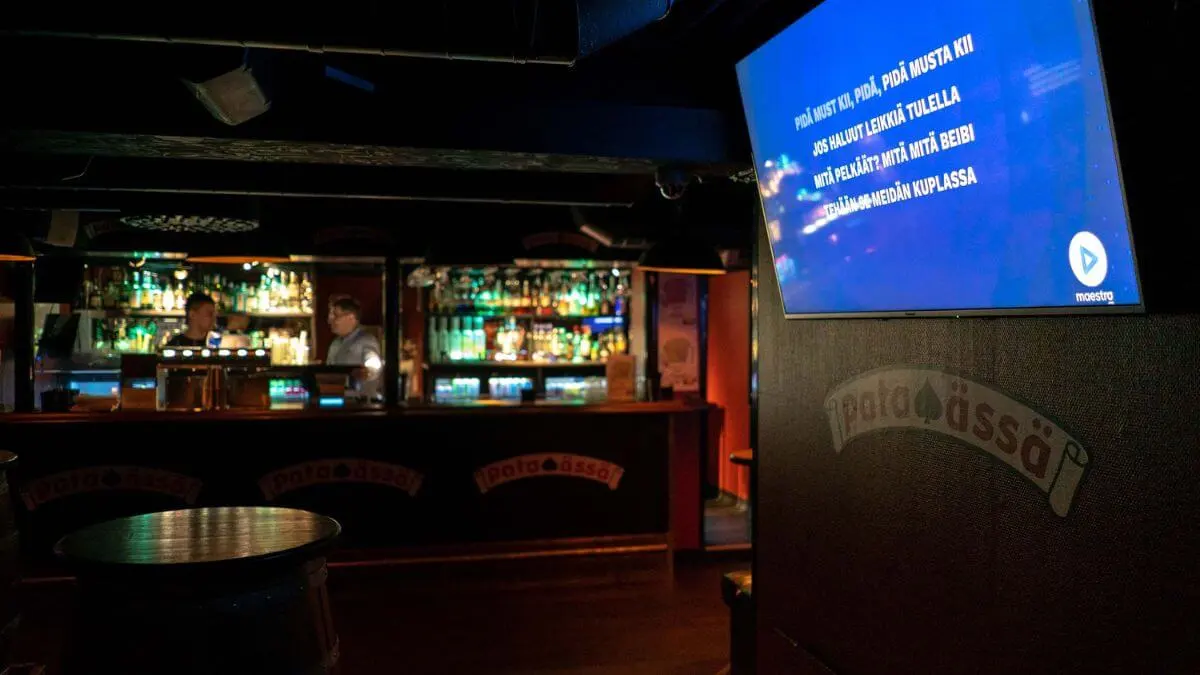 Indoor of the karaoke bar. In the background, there is a bar counter, and on the wall, there is a TV screen playing karaoke.